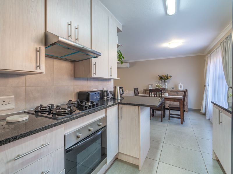 Open-plan kitchen and dining area featuring light wood cabinetry, granite countertops, gas hob, built-in oven, and tiled flooring throughout.