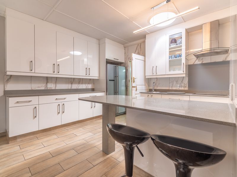 Modern kitchen featuring white high-gloss cabinetry, stone countertops, a central island, and stylish tiled flooring with integrated extractor fan.