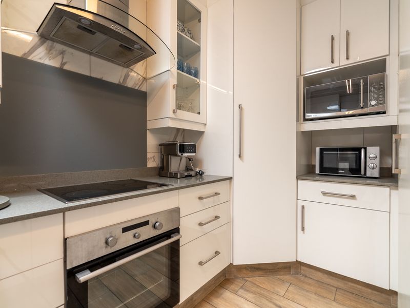 Modern kitchen featuring white cabinetry, stone countertops, built-in oven, electric hob, extractor fan, and integrated microwave with a clean, contemporary finish.