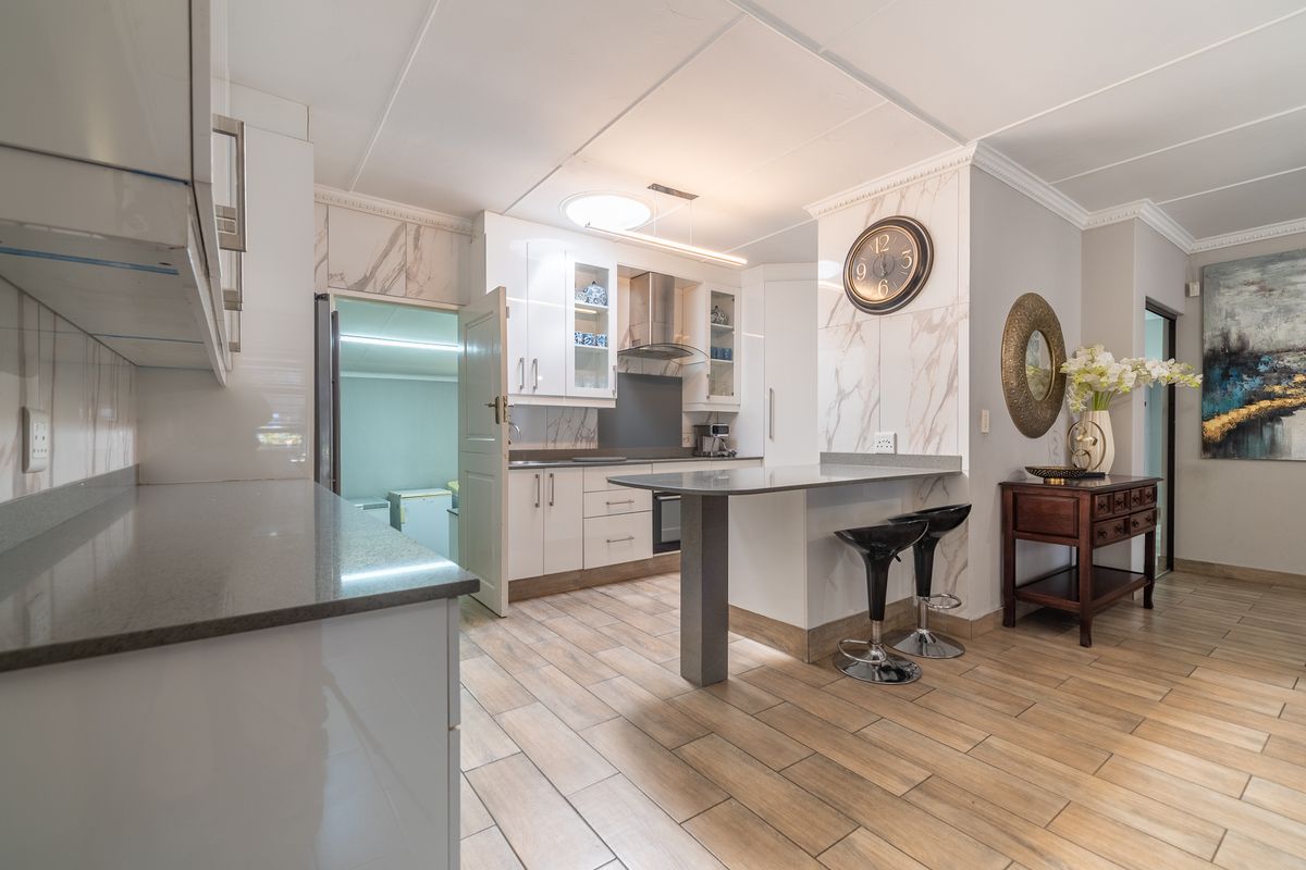 Modern kitchen featuring white cabinetry, quartz countertops, a breakfast bar, and marble-look splashback, complemented by wood-look tiled flooring.
