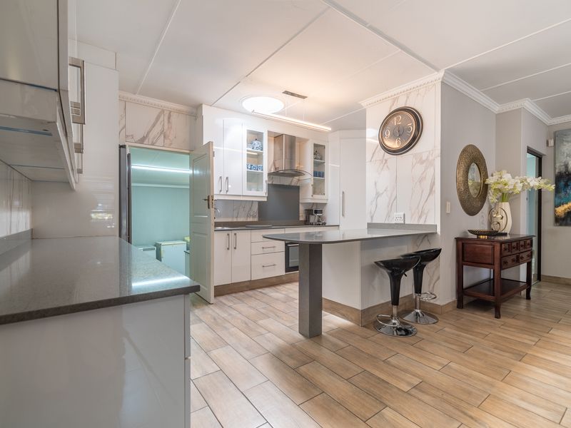 Modern kitchen featuring white cabinetry, quartz countertops, a breakfast bar, and marble-look splashback, complemented by wood-look tiled flooring.