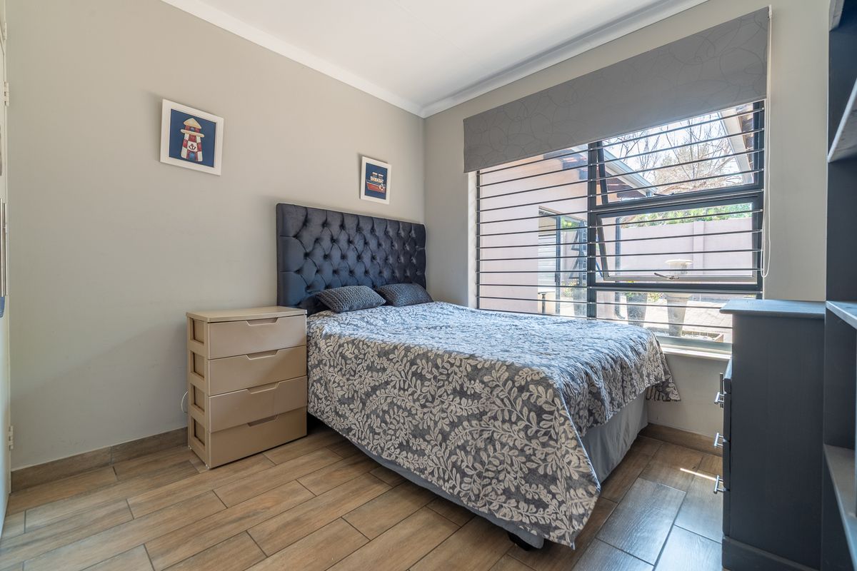 A well-maintained bedroom featuring modern tiled flooring, neutral wall tones, and large aluminium-framed windows with fitted horizontal blinds.