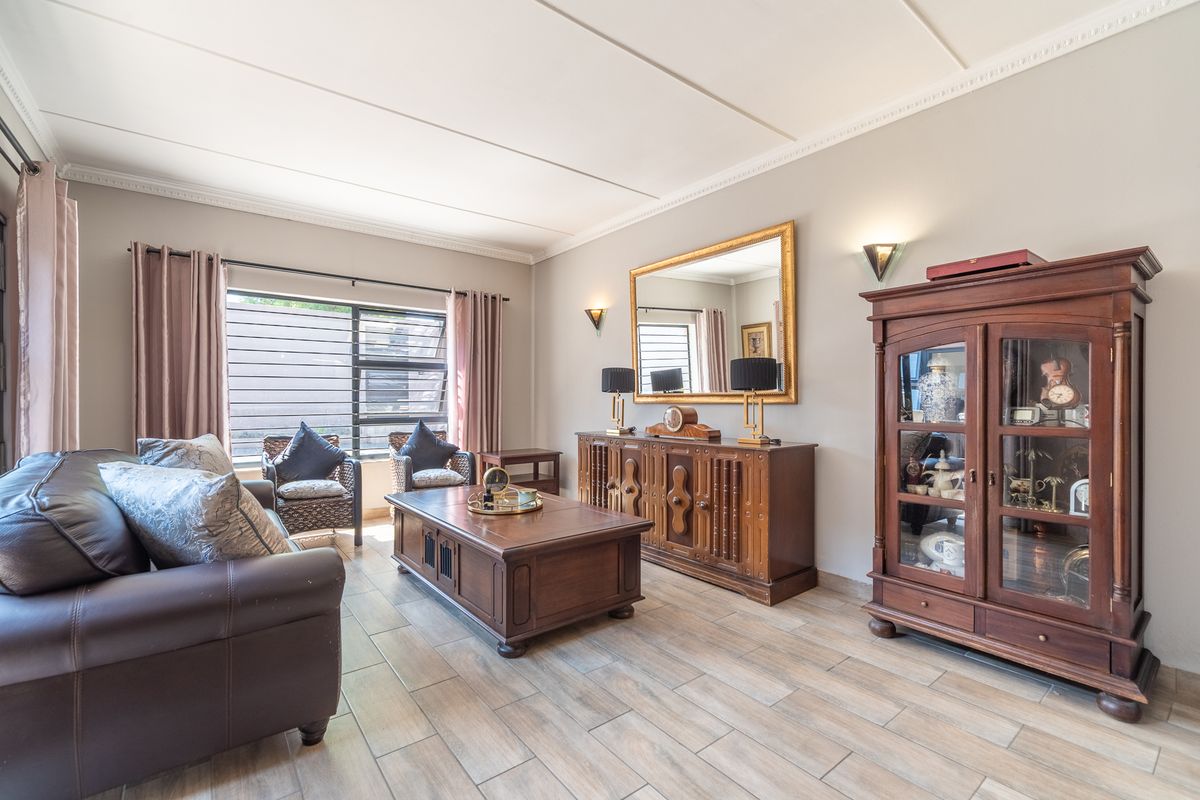 A well-maintained living room featuring neutral walls, tiled flooring, and a coved ceiling with integrated wall lighting.