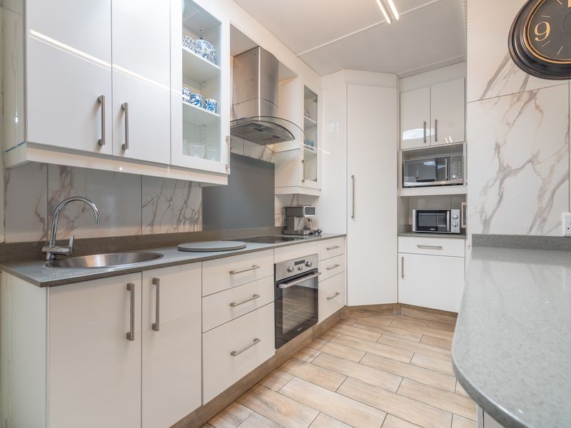 Modern kitchen featuring white cabinetry, stone countertops, marble-look splashbacks, built-in oven, extractor fan, and durable tiled flooring.