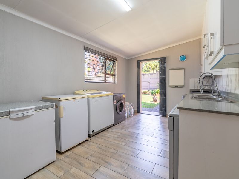 Functional laundry room featuring tiled flooring, built-in cabinetry, countertop space with a sink, and direct access to the rear garden.