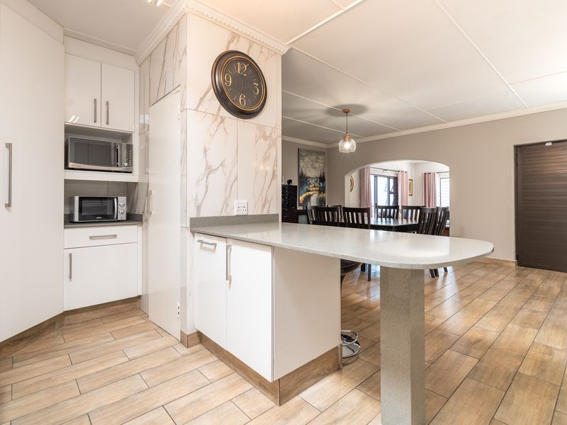 Modern open-plan kitchen featuring white cabinetry, stone countertops, a breakfast bar, and tiled flooring, seamlessly flowing into the adjacent dining area.