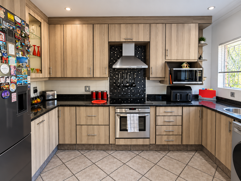 Modern kitchen featuring light wood-grain cabinetry, black granite countertops, stainless steel appliances, and a decorative mosaic tile backsplash.