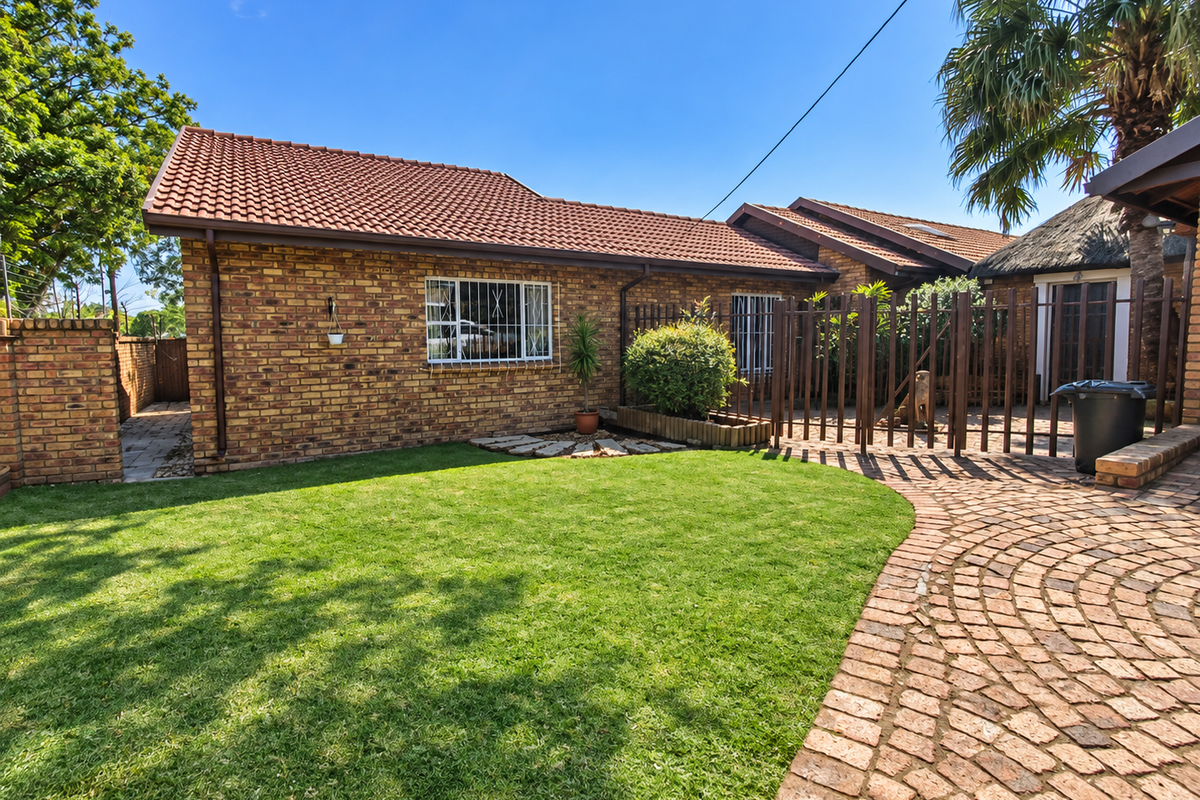 A well-maintained rear exterior view featuring a face brick facade, tiled roof, paved pathway, and a neat lawn area.