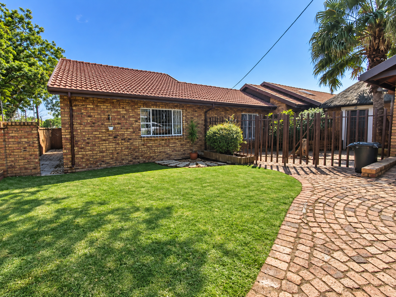 A well-maintained rear exterior view featuring a face brick facade, tiled roof, paved pathway, and a neat lawn area.