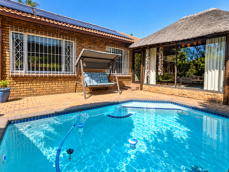Outdoor pool area featuring brick paving, a thatched-roof structure, and solar panels installed on the main house roof.