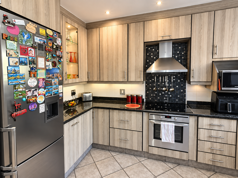 Modern kitchen featuring wood-grain cabinetry, black granite countertops, a stainless steel oven with extractor fan, and a stylish black mosaic tile backsplash.