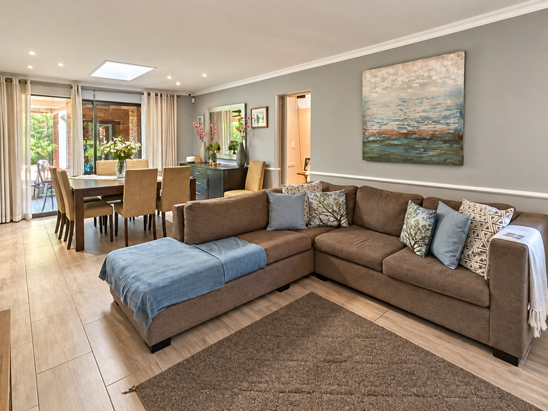 Spacious open-plan living and dining area featuring modern tiled flooring, recessed lighting, a skylight, and seamless access to the outdoor patio through sliding doors.