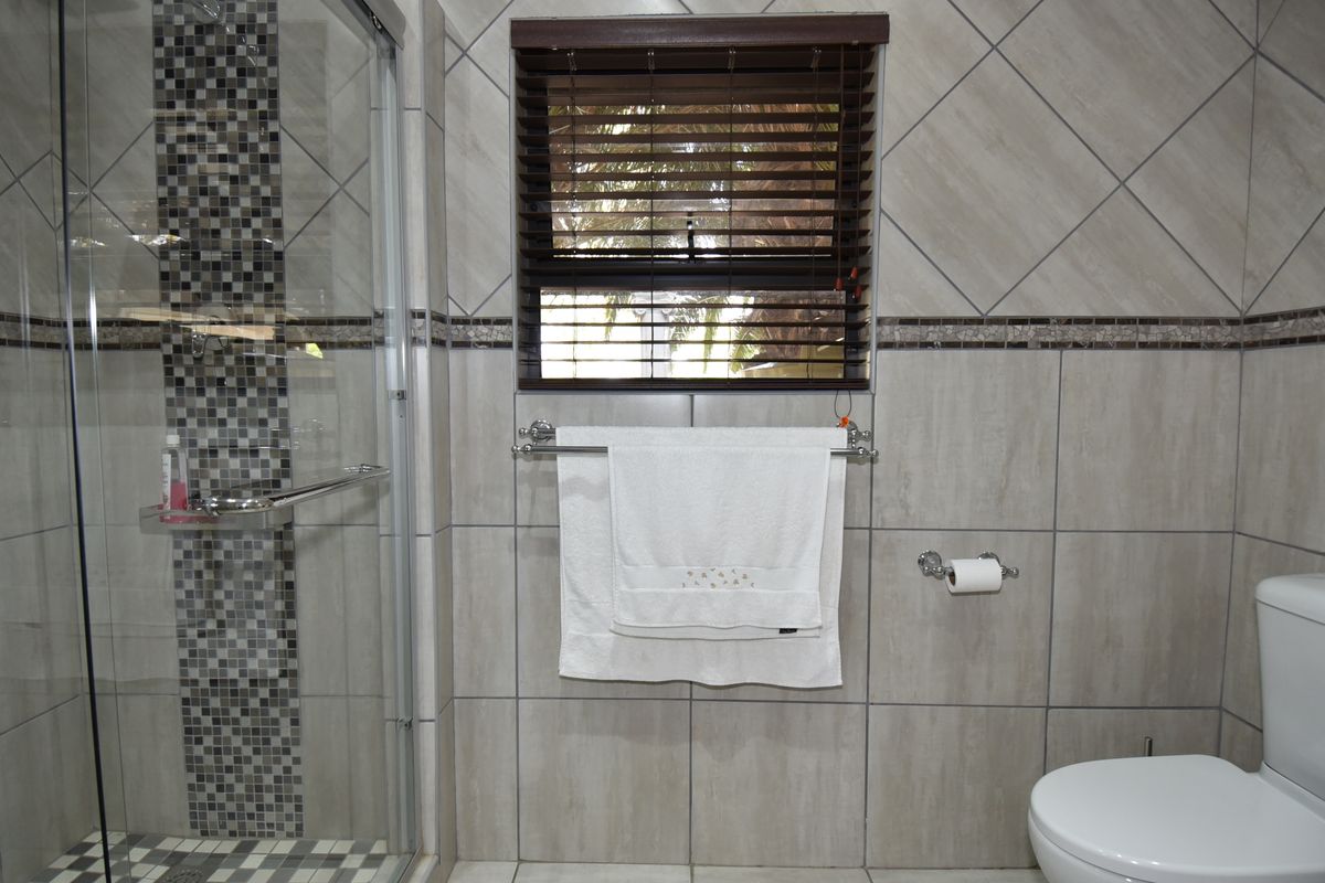 A well-maintained bathroom featuring a glass-enclosed shower with mosaic tile accents, neutral ceramic wall tiling, and a modern toilet.