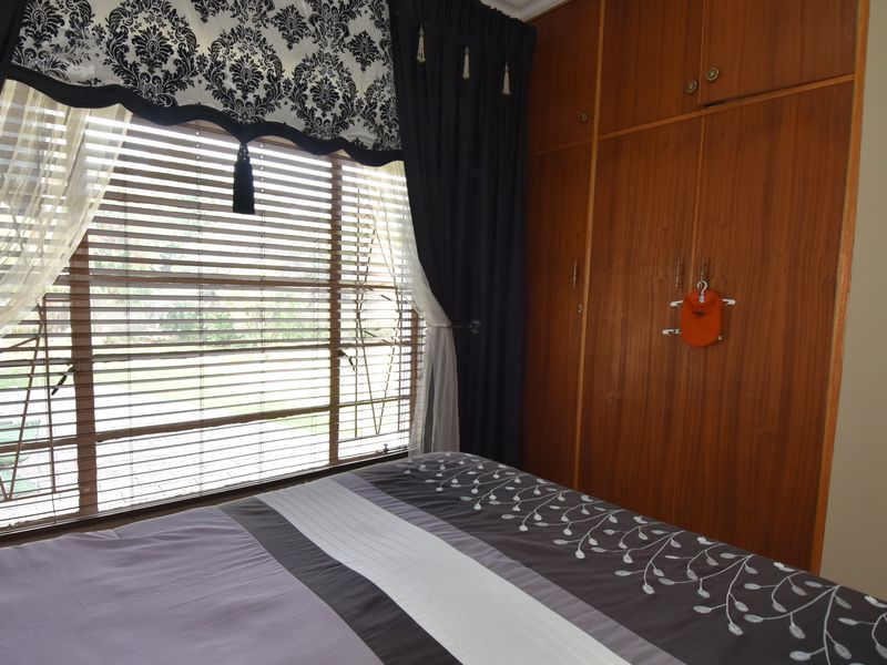 A bedroom featuring built-in wooden cupboards and venetian blinds, offering a functional space with natural light.