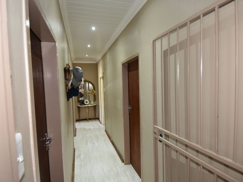 A clean, well-lit hallway featuring laminate flooring, a tongue and groove ceiling, and a fitted security gate.