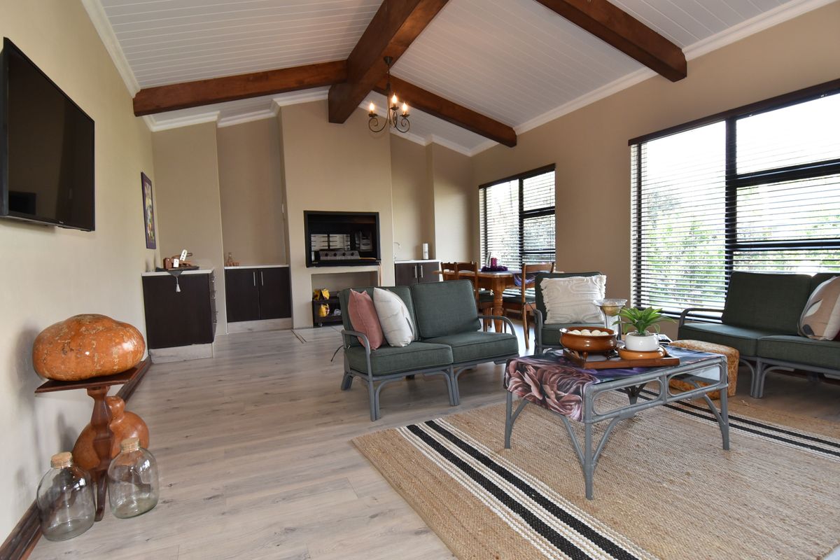 Spacious living room featuring exposed timber ceiling beams, laminate flooring, a built-in fireplace, and large windows with venetian blinds.
