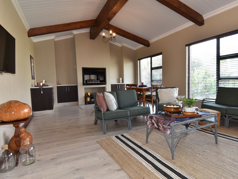 Spacious living room featuring exposed timber ceiling beams, laminate flooring, a built-in fireplace, and large windows with venetian blinds.
