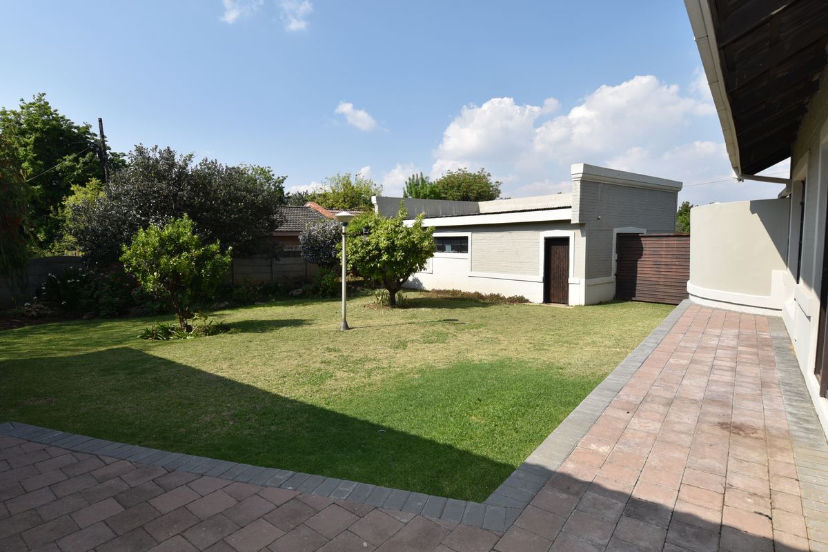 A well-maintained rear garden featuring a paved patio area, manicured lawn, and a detached outbuilding with a secure entrance.