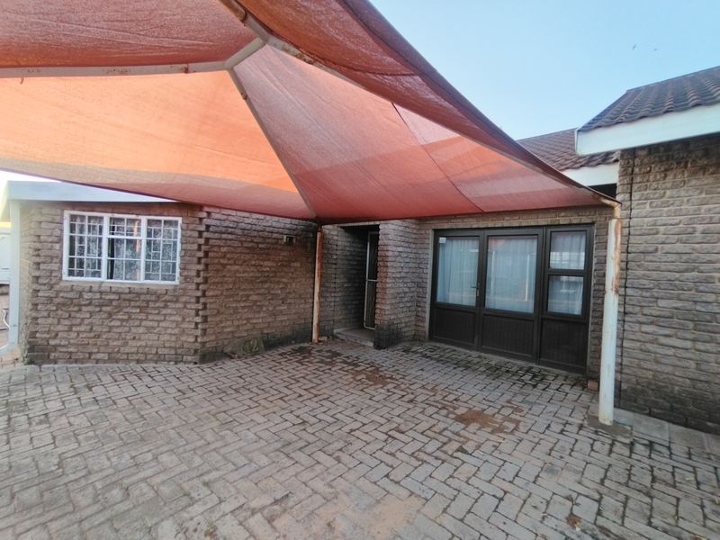 Front exterior view featuring a paved driveway, brick facade, and a large shade sail covering the entrance area.