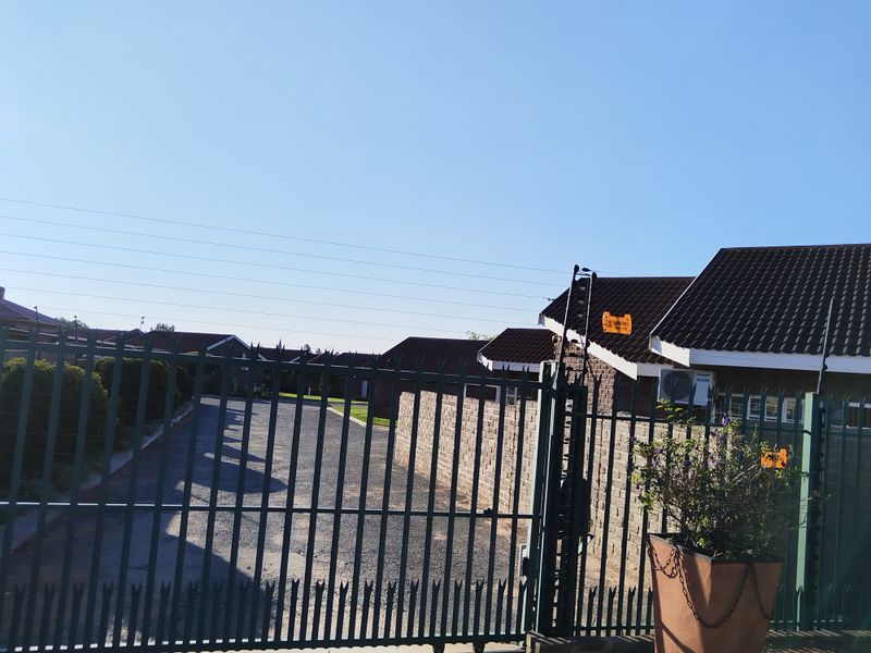 View of the property entrance featuring a metal security gate, electric fencing, and a gravel driveway leading to the residential units.