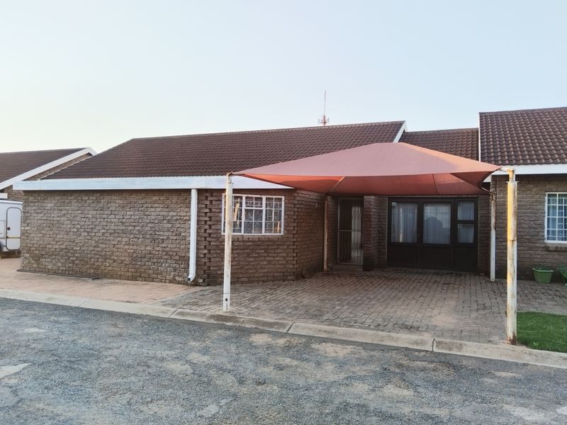 Front exterior view of a face brick house featuring a paved driveway and a shade sail carport structure.
