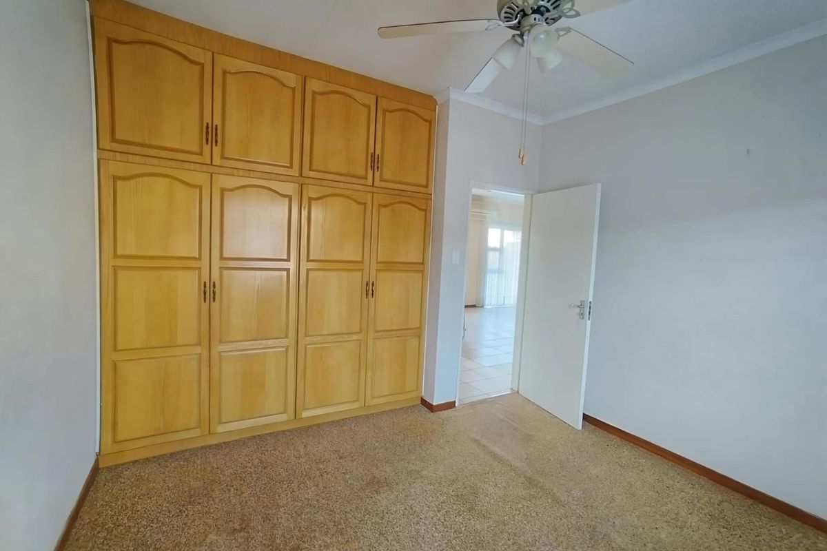 A vacant bedroom featuring built-in wooden cupboards, a ceiling fan, and carpeted flooring, offering a neutral space ready for personalization.