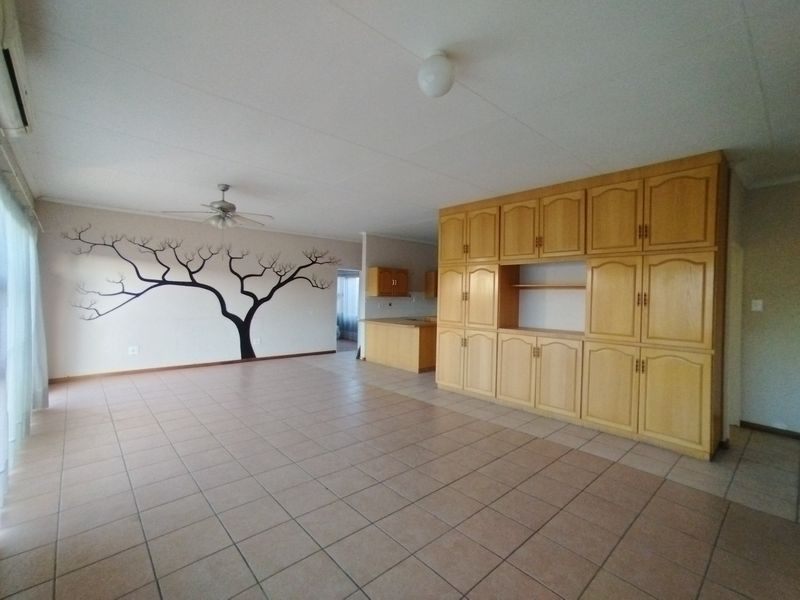 Spacious open-plan living area featuring neutral tiled flooring, extensive built-in cabinetry, and a ceiling fan, offering a versatile layout for modern living.