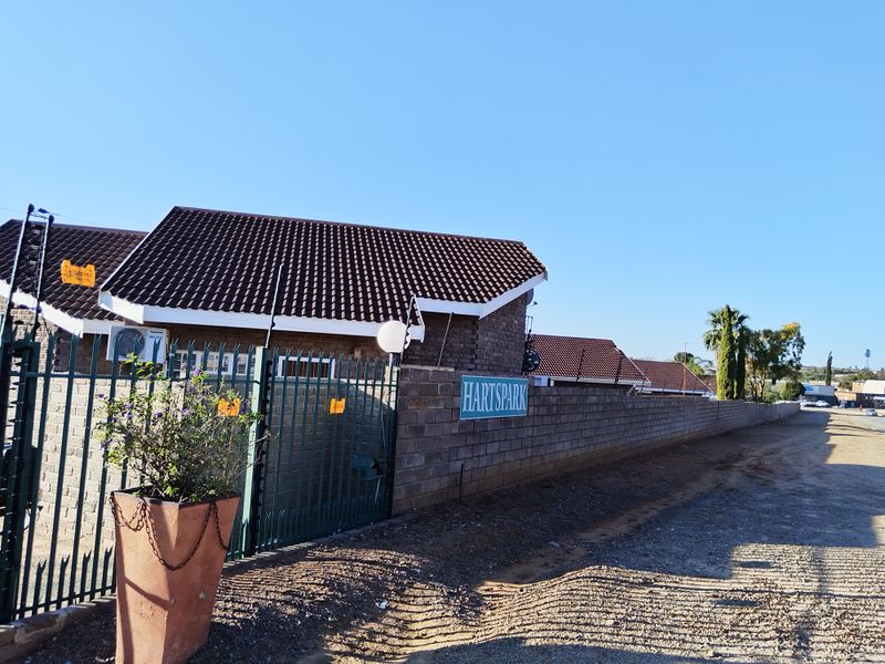 Street-level view of the property entrance featuring a face brick boundary wall, tiled roof structure, and secure perimeter fencing with electric security wires.