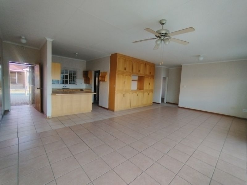 Spacious open-plan living and kitchen area featuring tiled flooring, built-in cabinetry, and a ceiling fan, offering a versatile layout for modern living.