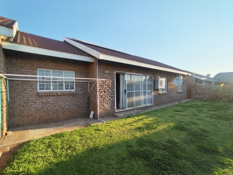 Rear view of a face brick house featuring a tiled roof, sliding door access, security bars, and a private lawn area.