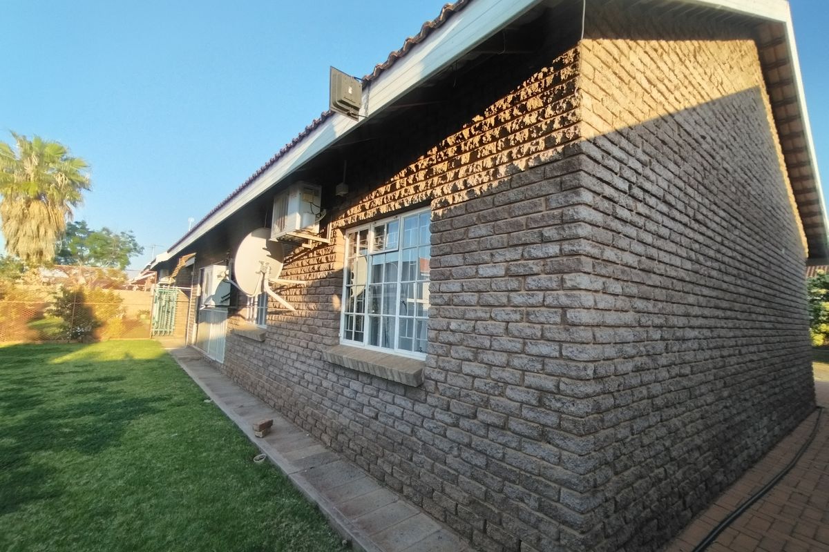 Rear exterior view of the house featuring face brick walls, tiled roofing, aluminium window frames, and a paved walkway alongside a lawn.