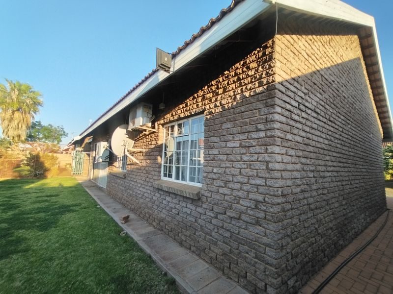 Rear exterior view of the house featuring face brick walls, tiled roofing, aluminium window frames, and a paved walkway alongside a lawn.