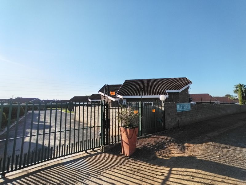 Front entrance view of the Hartspark residential complex featuring a secure metal gate, perimeter walling with electric fencing, and a paved driveway.