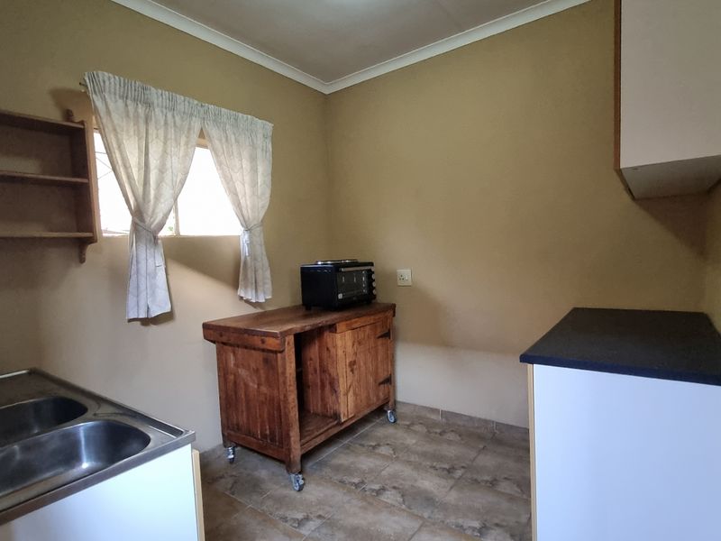 A functional kitchen area featuring tiled flooring, a double bowl stainless steel sink, and basic cabinetry, offering potential for modernization and aesthetic updates.