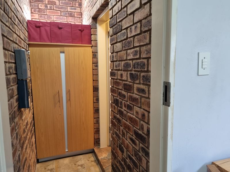 A narrow hallway featuring exposed brick walls and tiled flooring, providing access to adjacent rooms.