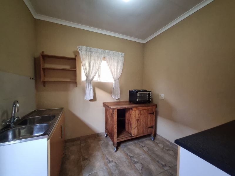 A functional kitchen area featuring a double bowl stainless steel sink, tiled flooring, and wall-mounted shelving, offering a practical layout for food preparation.