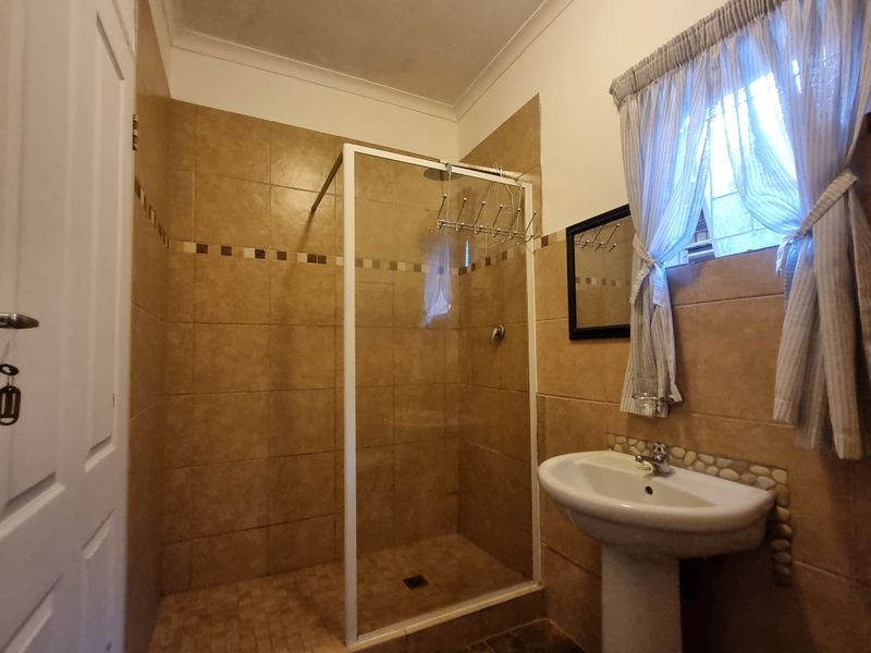A functional bathroom featuring a walk-in shower enclosure, pedestal basin, and neutral floor-to-ceiling wall tiling.