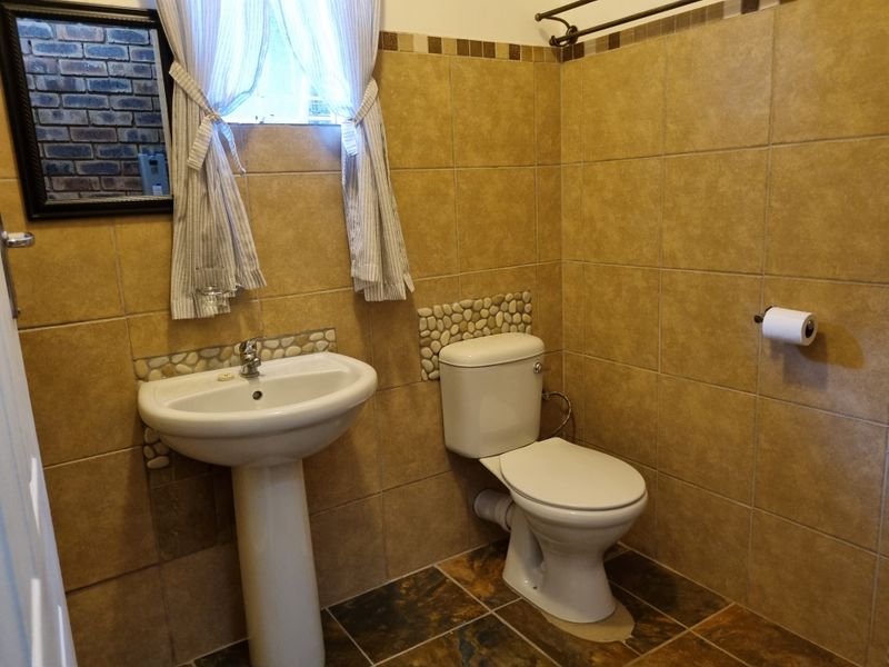 A functional bathroom featuring a pedestal basin, toilet, and earth-toned wall and floor tiling with decorative pebble accents.