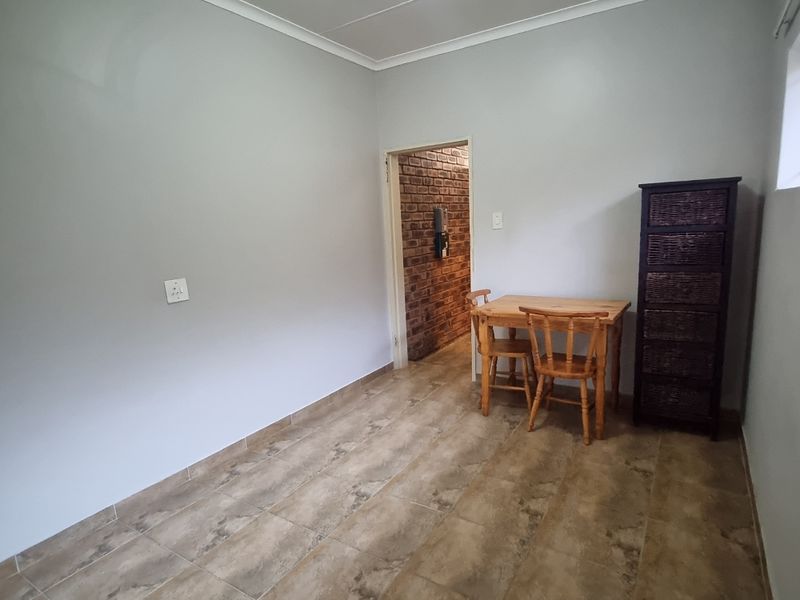 A simple living area featuring neutral painted walls, tiled flooring, and a doorway leading to an exposed brick interior space.