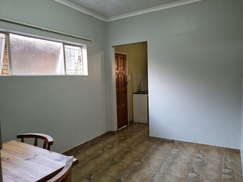 A simple, neutral living area featuring tiled flooring and coved ceilings, with a doorway leading to an adjacent kitchen space.