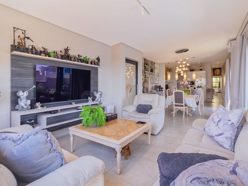 Spacious open-plan living and dining area featuring tiled flooring, recessed lighting, and a modern built-in media unit with direct access to outdoor space.