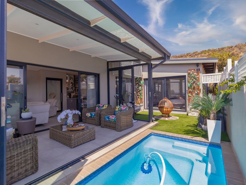 A well-maintained outdoor entertainment area featuring a swimming pool, covered patio with sliding glass doors, and artificial turf landscaping.
