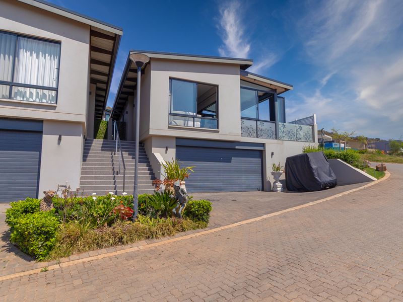 Modern multi-level residential facade featuring a double garage, paved driveway, and an elevated balcony with glass balustrades.