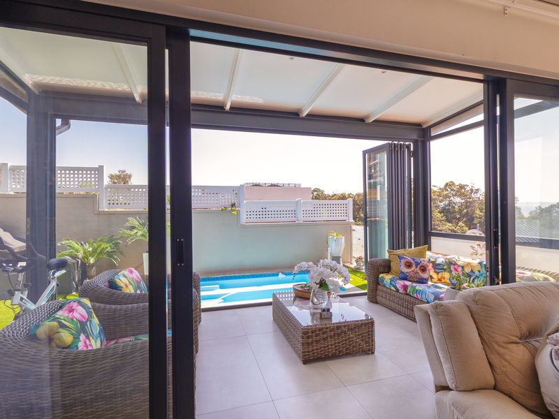A covered patio area featuring tiled flooring and large sliding glass doors, overlooking a private swimming pool and landscaped garden area.