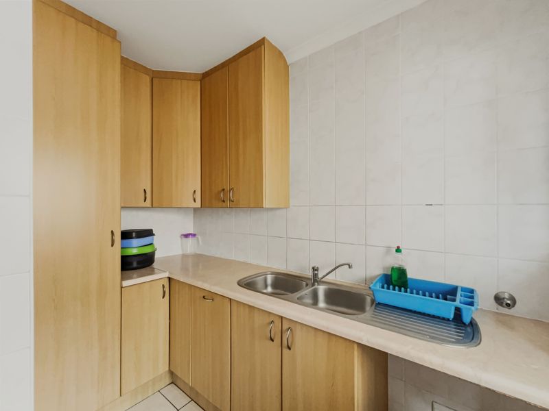 A functional scullery area featuring light wood-finish cabinetry, laminate countertops, and a double bowl stainless steel sink with tiled splashback.