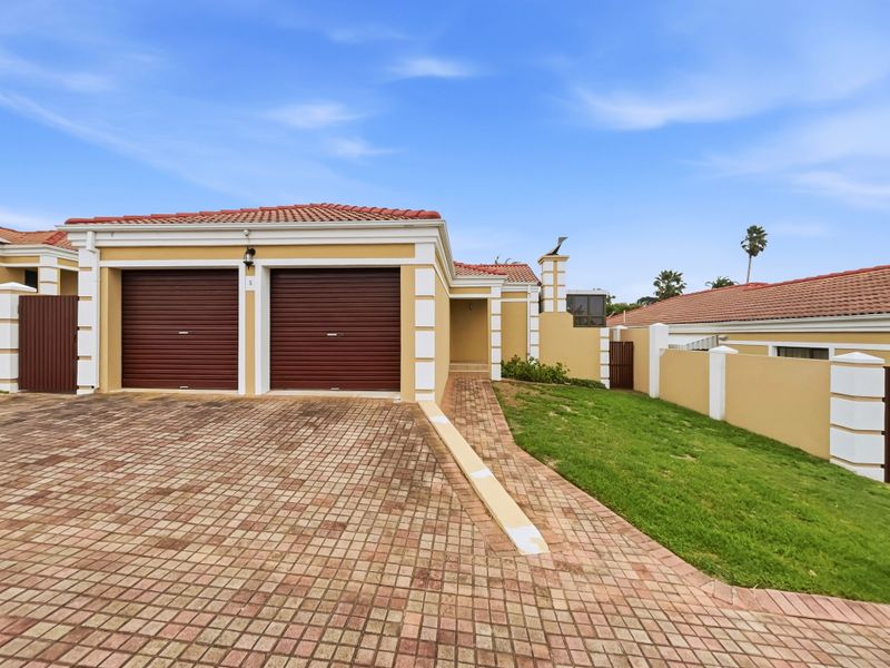 Front elevation of a cluster home featuring a double garage with roll-up doors, a paved driveway, and a well-maintained boundary wall.