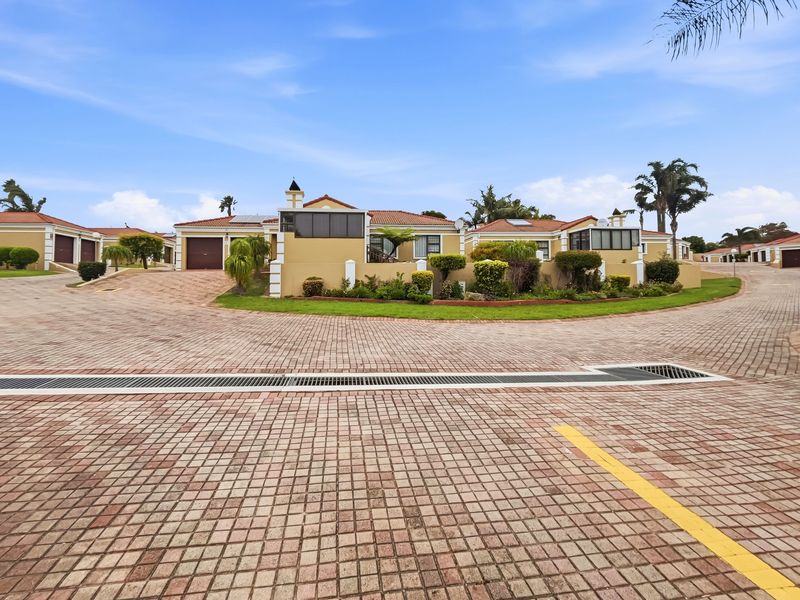 A view of the front exterior of a cluster home featuring a paved driveway, garage, and enclosed patio area within a well-maintained estate.