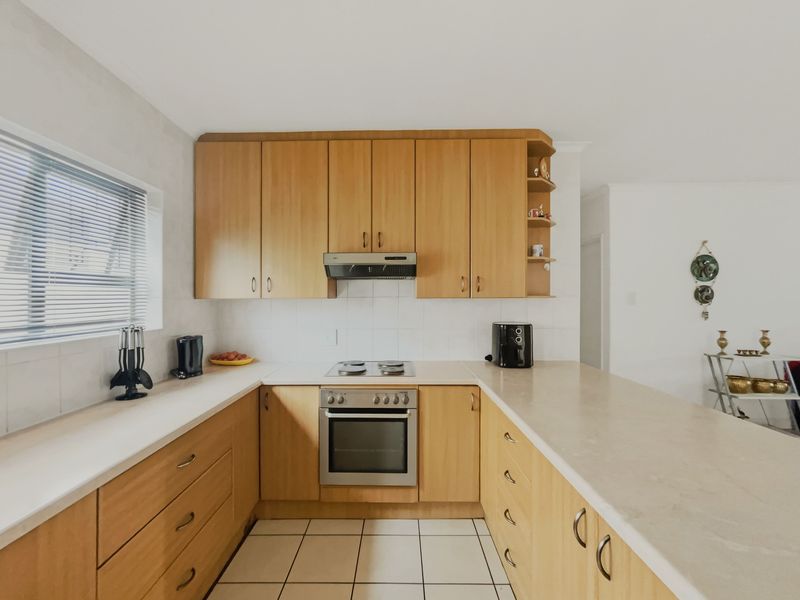 A functional kitchen featuring light wood cabinetry, laminate countertops, a built-in oven with hob, and tiled flooring.