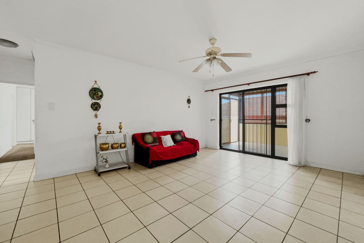 A spacious living area featuring neutral tiled flooring, a ceiling fan, and a sliding glass door providing access to the outdoor patio.
