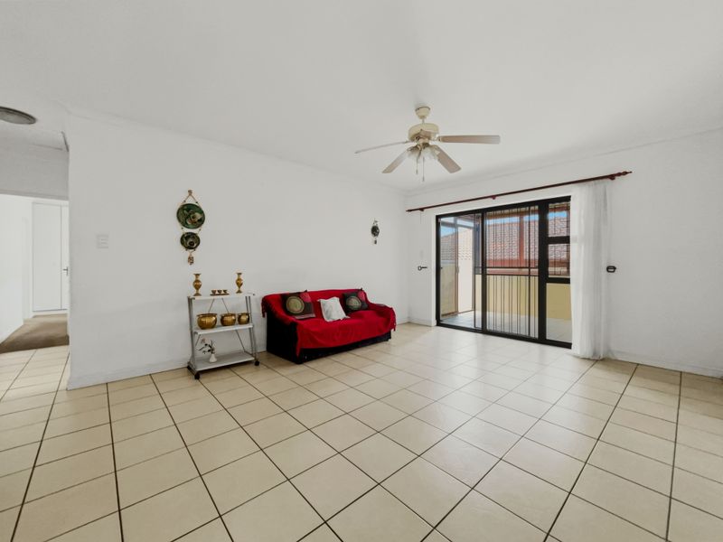A spacious living area featuring neutral tiled flooring, a ceiling fan, and a sliding glass door providing access to the outdoor patio.